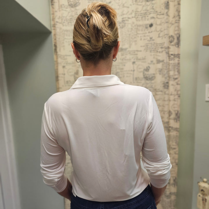 Person wearing a white shirt and blue jeans standing in a room with patterned wallpaper.