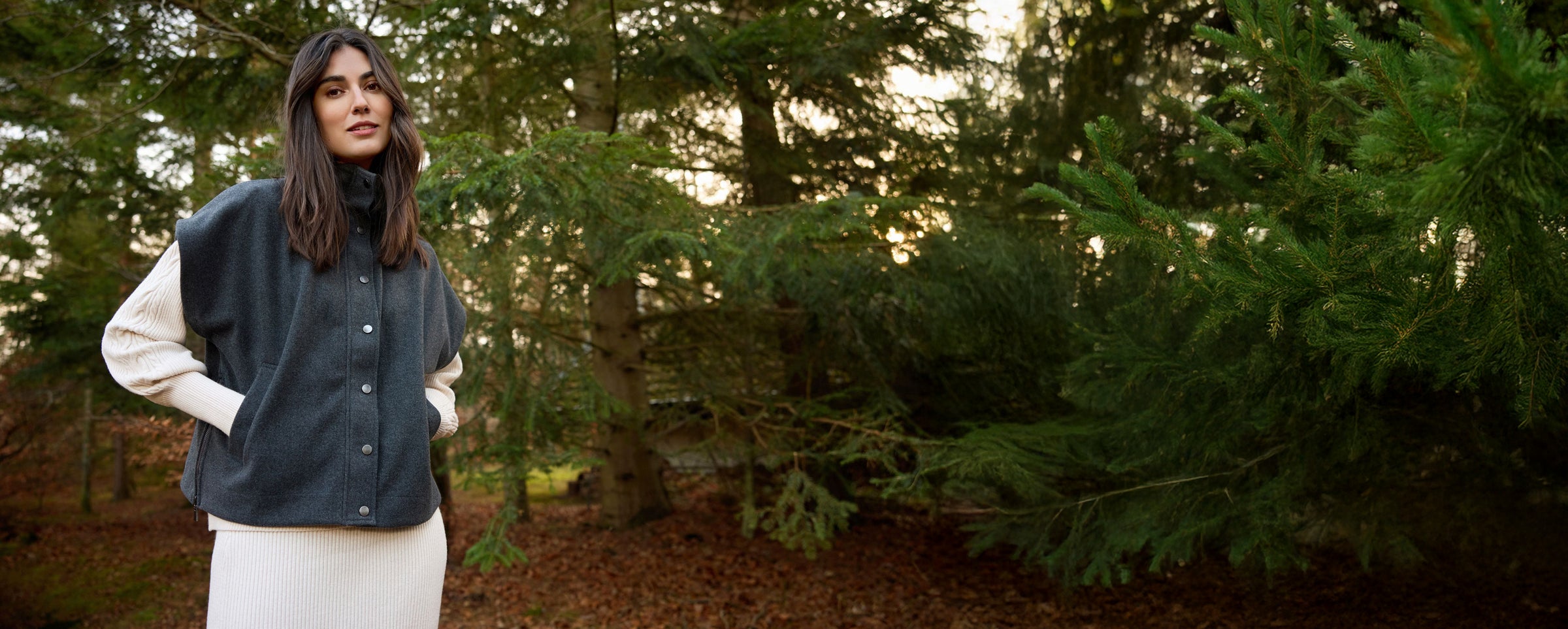 Woman wearing a dark vest over a white shirt in a forest setting