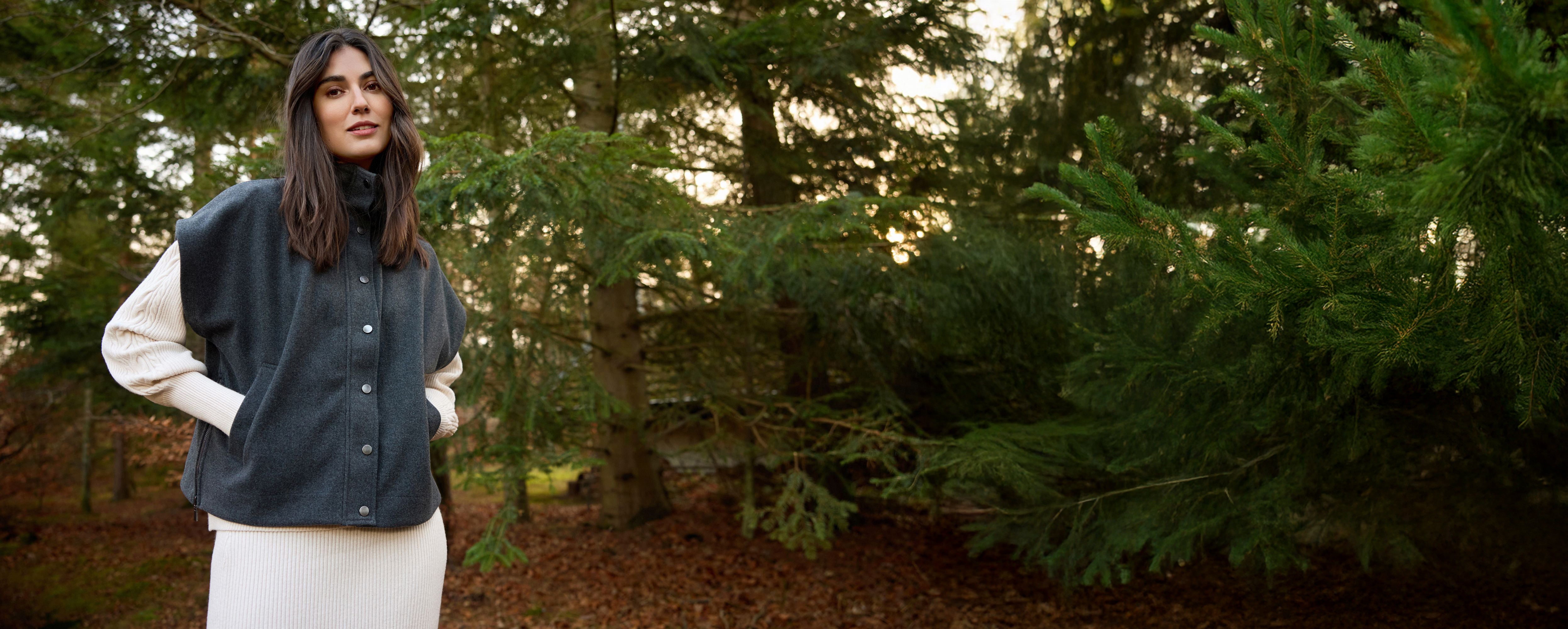 Woman wearing a dark vest over a white shirt in a forest setting