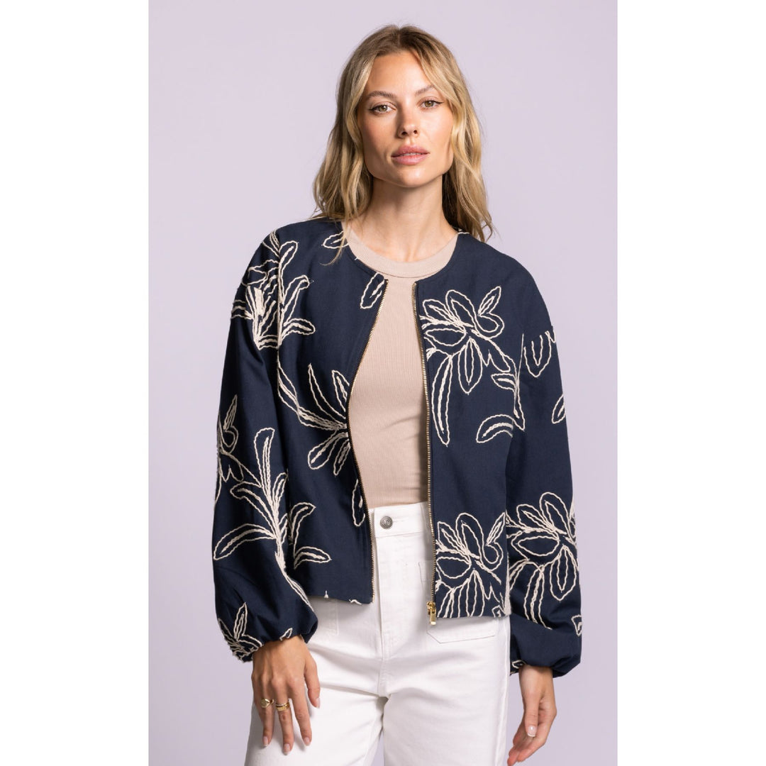 Woman wearing a navy blue floral-patterned jacket on a light purple background