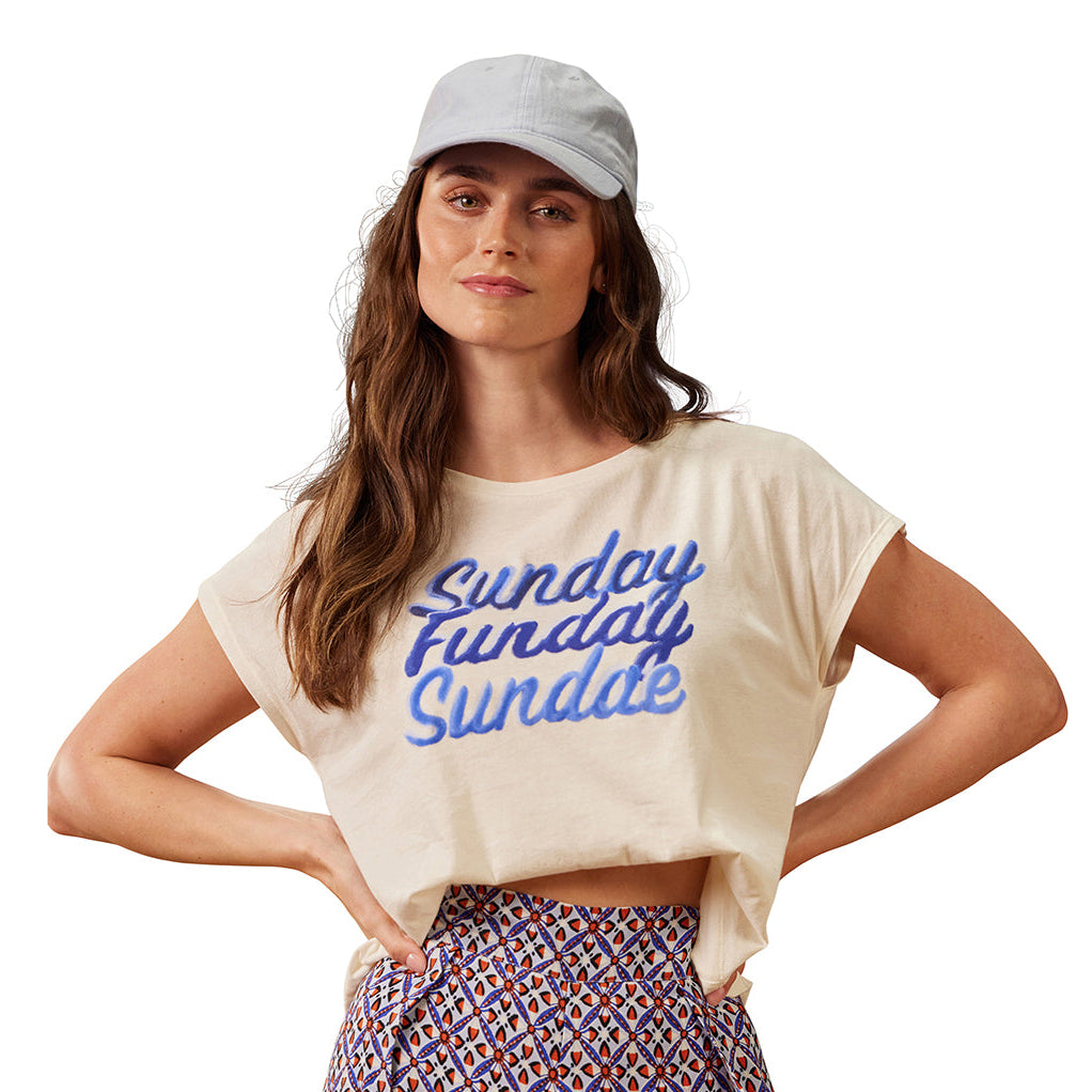 Woman wearing a white t-shirt with 'Sunday Funday' text and patterned pants on a white background